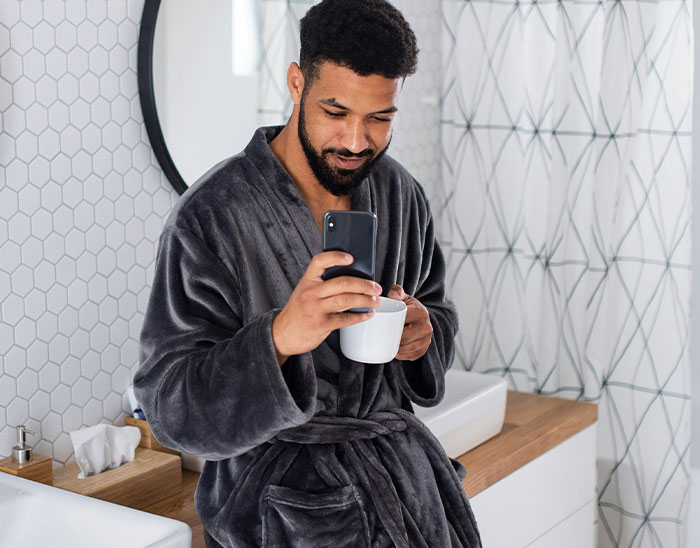 Hombre con bata gris tomando café y usando el celular, ilustrando momentos de abogados y clientes sorprendentes.