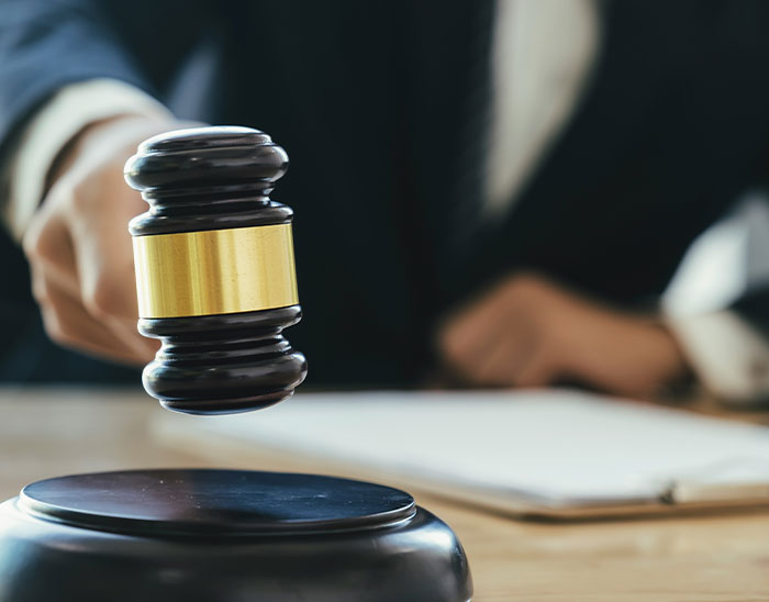 Mazo de juez en primer plano con abogado en fondo desenfocado representando abogados y casos legales.