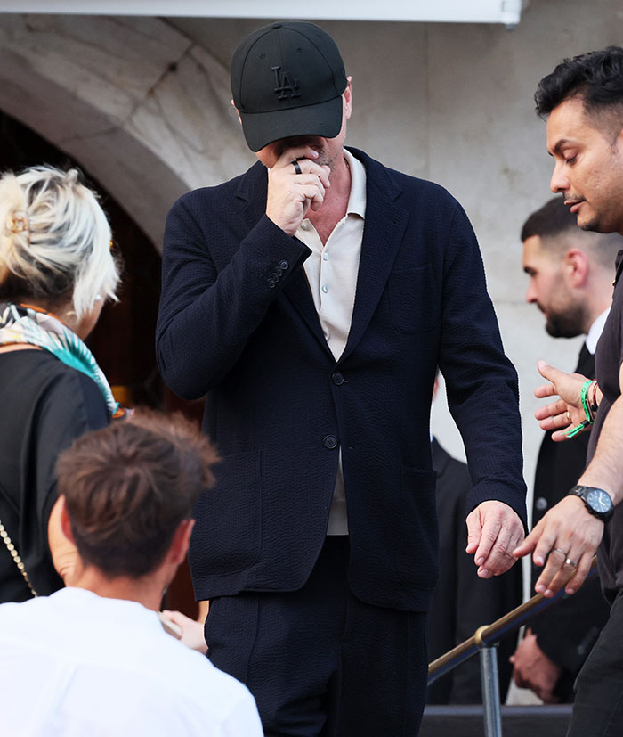 Hombre con gorra negra y traje oscuro entre invitados en evento de celebridades peor vestidas en boda de Jeff Bezos.