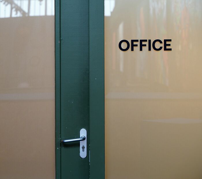 Puerta de oficina verde con ventana translúcida y palabra office, simbolizando conversaciones privadas terroríficas escuchadas.