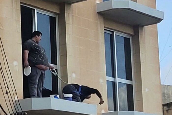 Hombre parado en balcón mientras otro limpia ventanas, ilustrando diferencias de salud y longevidad entre mujeres y hombres.