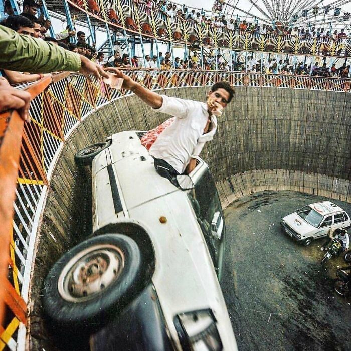 Hombre realizando una peligrosa acrobacia en auto dentro de un pozo con público observando, riesgo e impacto visual.