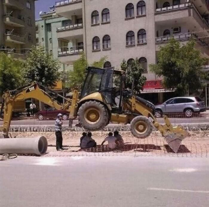Excavadora suspendida en obra con personas sentadas debajo, ilustrando razones por las que mujeres viven más que hombres.