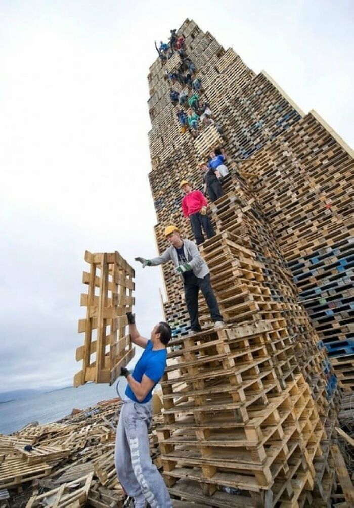 Personas apilando palets de madera en torre alta, simbolizando 30 razones por las que las mujeres viven más que los hombres.