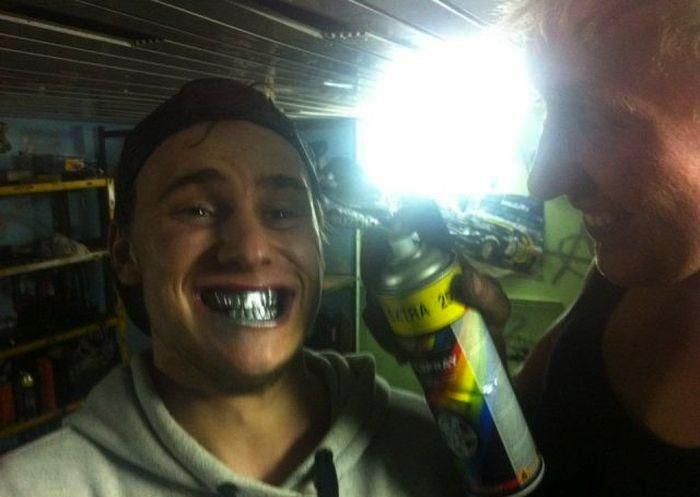 Joven sonriente con spray plateado en la boca mientras una mujer rocía pintura en un ambiente cerrado, mujeres viven más.