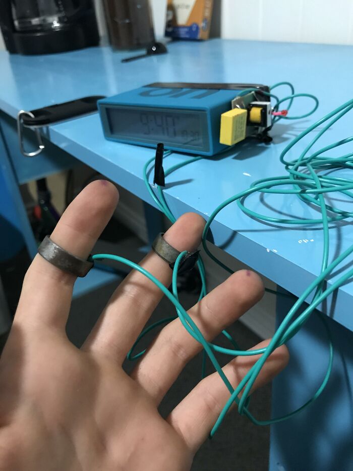 Mano con alambres y anillos metálicos conectados a un dispositivo en mesa azul relacionado con razones por las que las mujeres viven más.