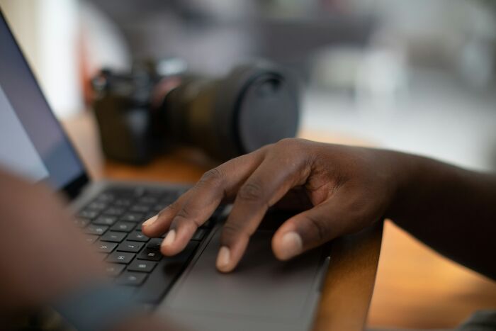 Mano negra escribiendo en laptop con cámara desenfocada al fondo, simbolizando experiencias online aterradoras.