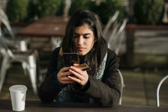 Mujer joven preocupada mientras usa su teléfono y tarjeta, simbolizando experiencias online aterradoras y riesgos digitales.