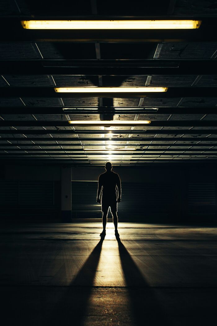 Persona de pie en sombra alargada en un estacionamiento oscuro, evocando experiencias online más aterradoras.