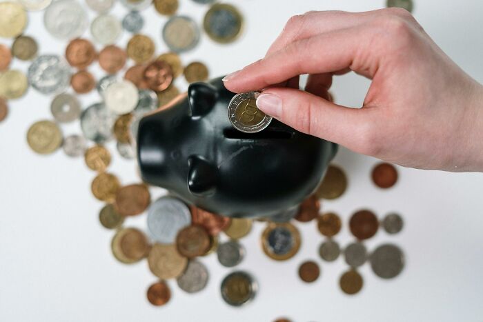 Mano femenina insertando moneda en alcancía negra, simbolizando consejos útiles para mujeres que viven solas y finanzas personales.