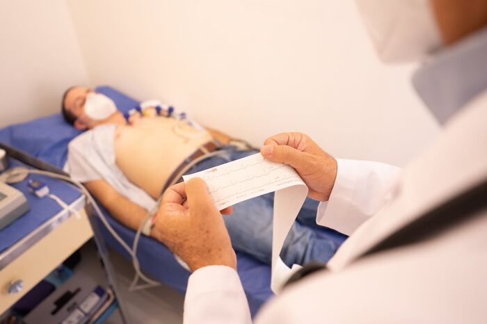 Paciente con mascarilla recibiendo examen médico mientras el doctor revisa resultados de análisis genéticos recientes.