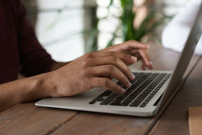 Manos escribiendo en laptop sobre mesa de madera, representando experiencias online más aterradoras compartidas.