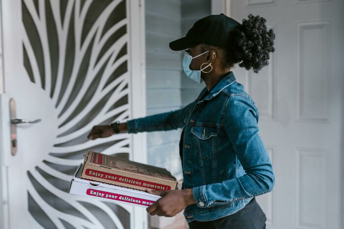 Mujer con cubrebocas y gorra entregando pizzas en la puerta, consejos útiles para mujeres que viven solas