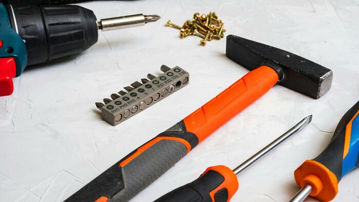 Herramientas básicas para mujeres que viven solas, mostrando destornilladores, martillo y tornillos sobre superficie blanca.
