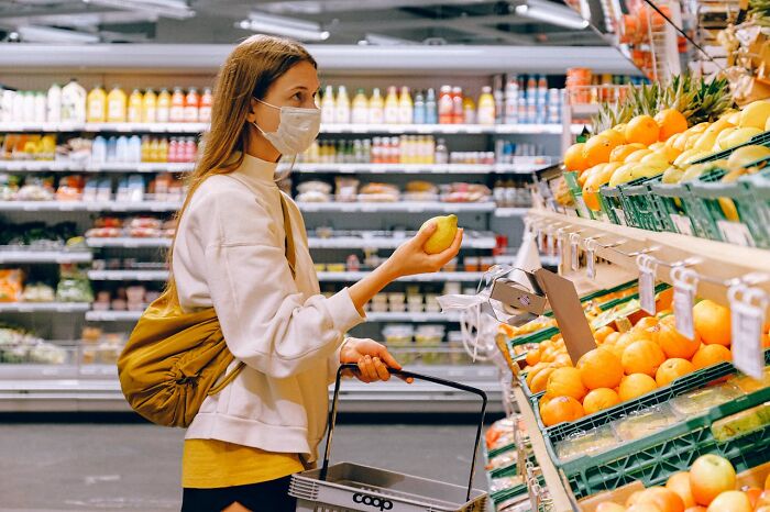 Mujer con mascarilla en supermercado eligiendo fruta, ilustrando momentos de corregir a la persona equivocada y fallar.