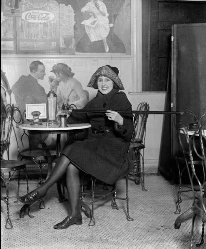 Mujer con sombrero y abrigo en café antiguo donde se muestra un lado distinto de la historia con detalles únicos.