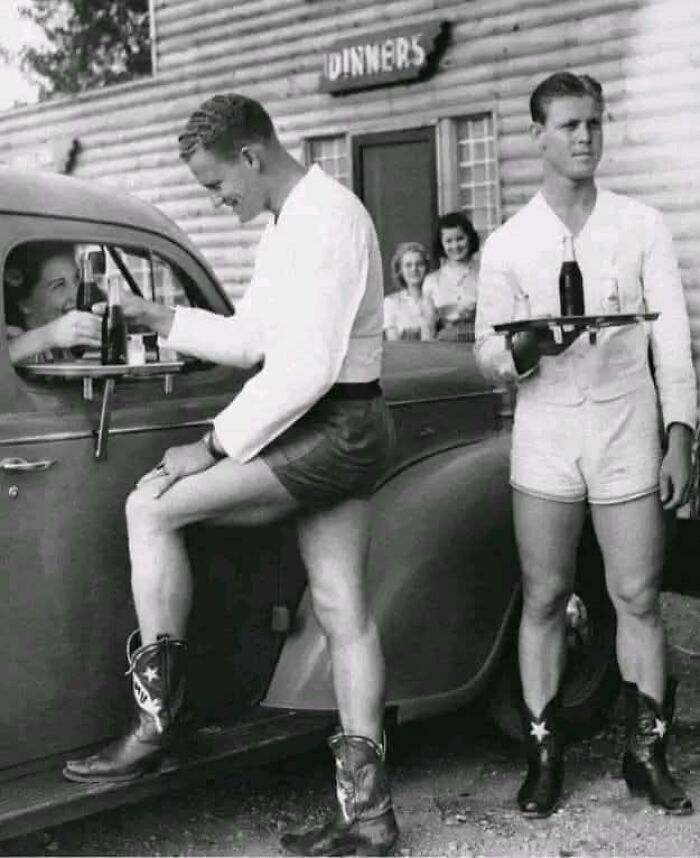 Hombres en ropa retro sirven bebidas en autos vintage mostrando un lado distinto de la historia.