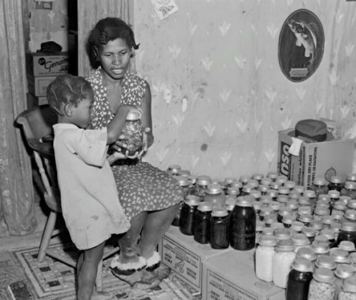 Madre e hijo con frascos de conservas caseras, mostrando un lado distinto de la historia en fotografía histórica.