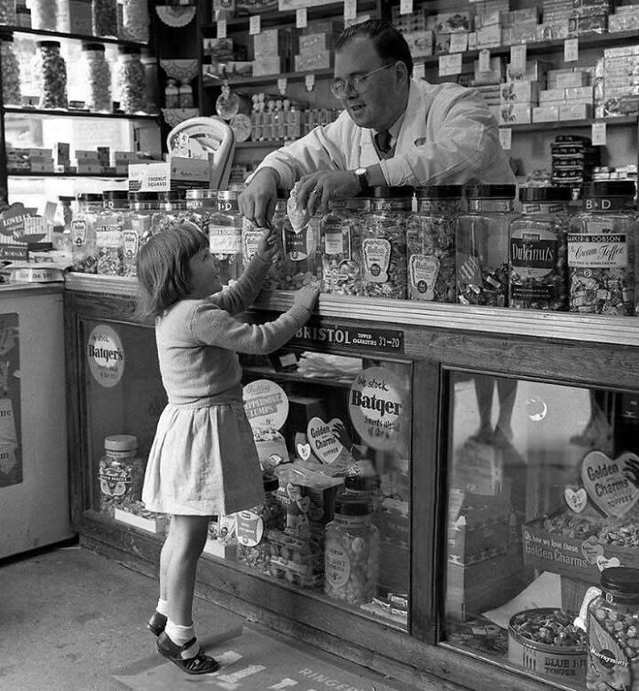Niña comprando dulces en una tienda antigua con hombre atendiendo, mostrando un lado distinto de la historia.