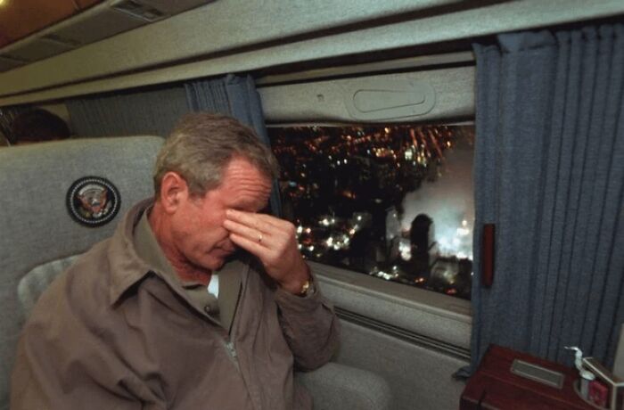 George W. Bush con gesto de preocupación en helicóptero mirando ángulo alternativo de zona afectada de evento histórico de noche.