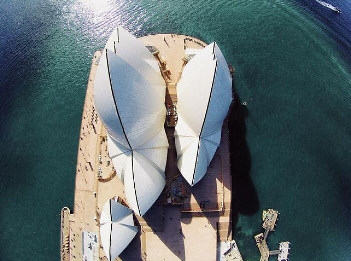 Vista aérea con ángulos alternativos del icónico edificio en la costa rodeado de agua y embarcaciones pequeñas.
