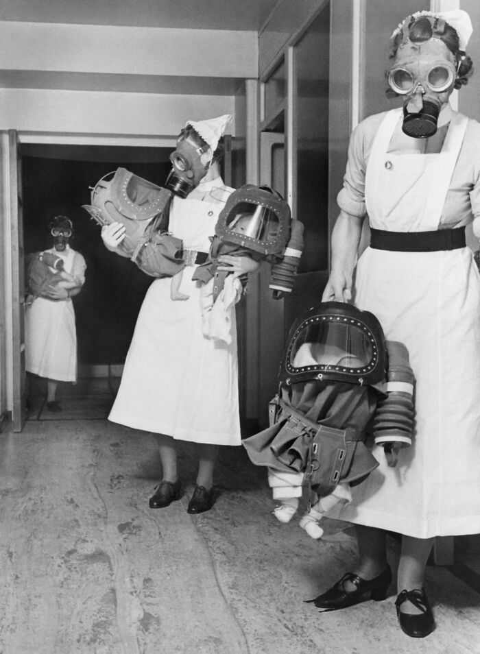 Enfermeras con mascarillas antigás sosteniendo muñecos con protección, foto inquietante del pasado.