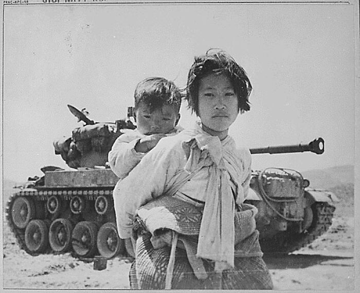 Niña cargando a un niño frente a un tanque militar en una foto del pasado inquietante y poderosa.