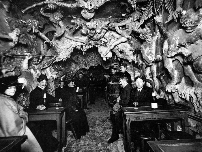 Foto antigua en bar con decoración inquietante de huesos y turistas vestidos de época disfrutando bebidas.
