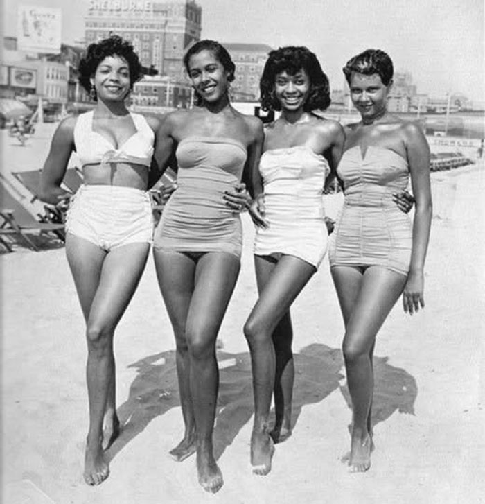 Cuatro mujeres sonrientes en trajes de baño vintage posando en la playa en una curiosa foto histórica del pasado inédito.