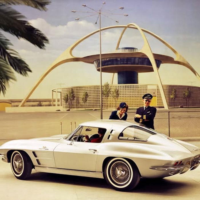 Coche clásico con piloto y azafata frente a arquitectura futurista en fotos históricas curiosas del pasado inédito.