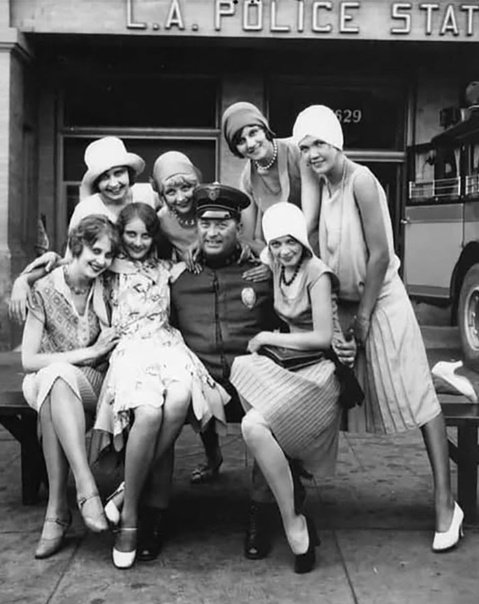 Policía de Los Ángeles rodeado de mujeres sonrientes en foto histórica curiosa con estilo de los años 20, representación del pasado inédito.
