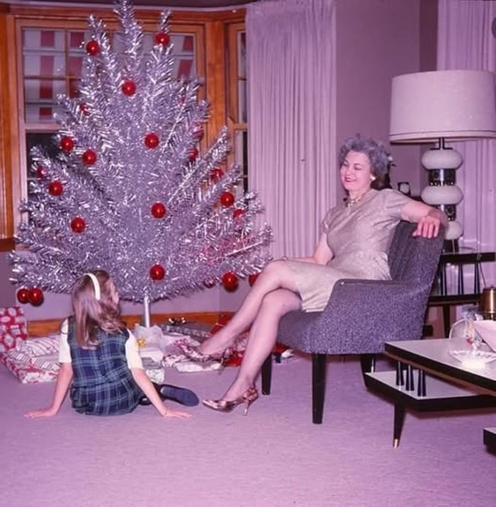 Mujer y niña sentadas junto a un árbol de Navidad plateado en sala vintage, foto histórica curiosa del pasado inédito.