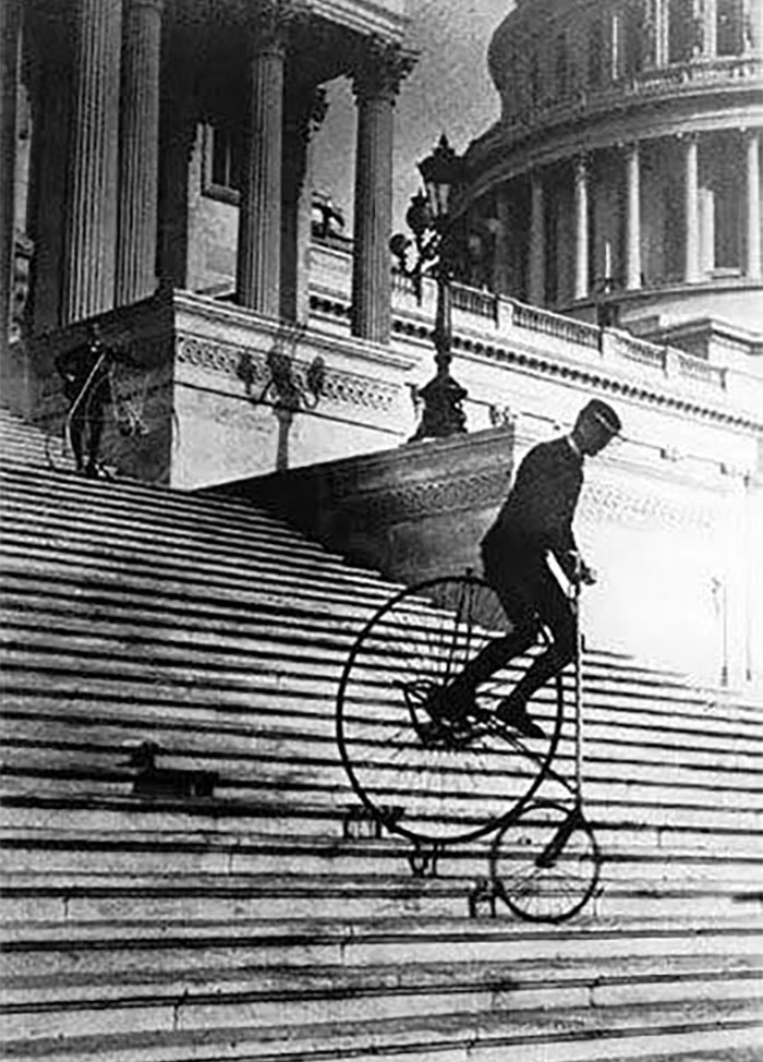 Hombre en bicicleta antigua bajando escaleras frente a edificio histórico en curiosas fotos históricas del pasado.