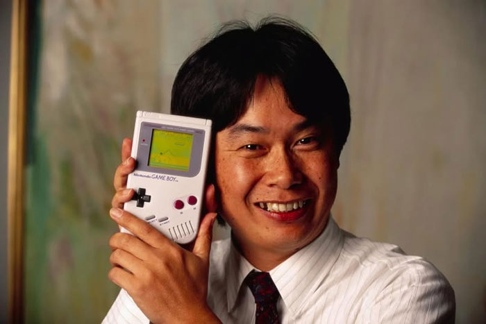 Hombre sonriente sosteniendo una consola Game Boy, foto histórica que muestra tecnología del pasado inédito.