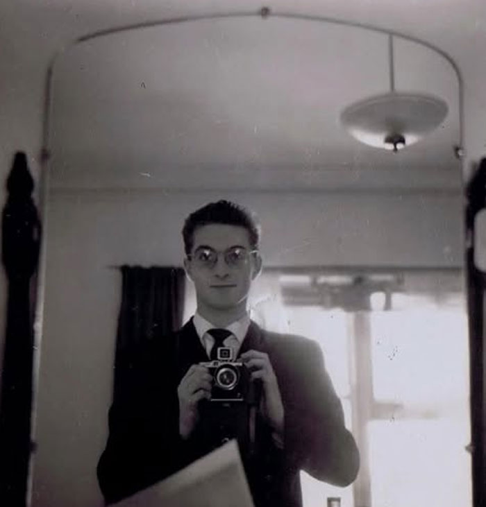 Hombre con gafas retratándose frente a un espejo con cámara antigua en foto histórica curiosa del pasado inédito.
