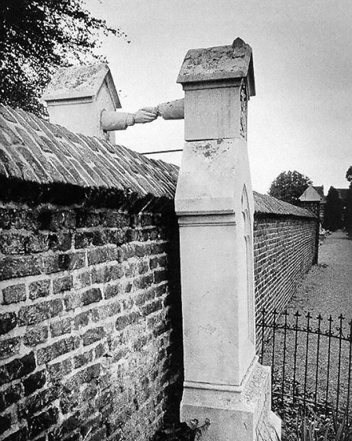 Manos saliendo de chimeneas conectadas sobre muro de ladrillos, foto histórica que muestra curiosidades arquitectónicas antiguas.
