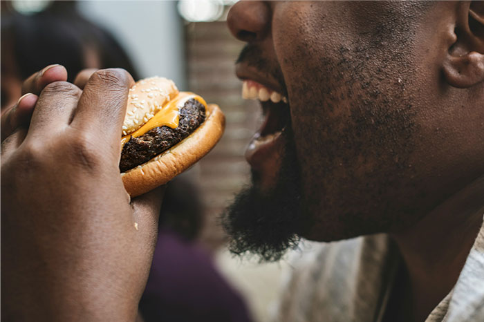 Hombre disfrutando una hamburguesa, ilustrando momentos de pérdida de atracción en pareja según mujeres entrevistadas.