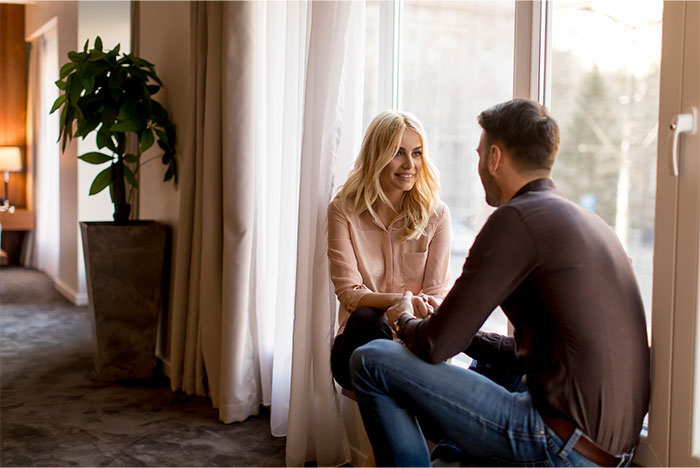 Pareja sentada cerca de una ventana, mostrando una conversación íntima sobre pérdida de atracción en la relación.