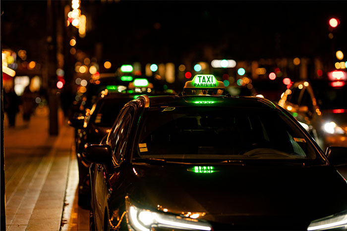 Taxi parisino estacionado en calle iluminada de noche, contexto ideal para citas terribles y experiencias de camareros.
