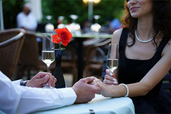 Pareja en una cita con copas de champagne en restaurante al aire libre, ilustrando citas terribles según camareros.