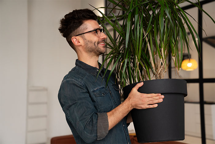 Hombre con gafas sosteniendo una maceta grande en interior, ilustrando relatos de citas terribles presenciadas por camareros.