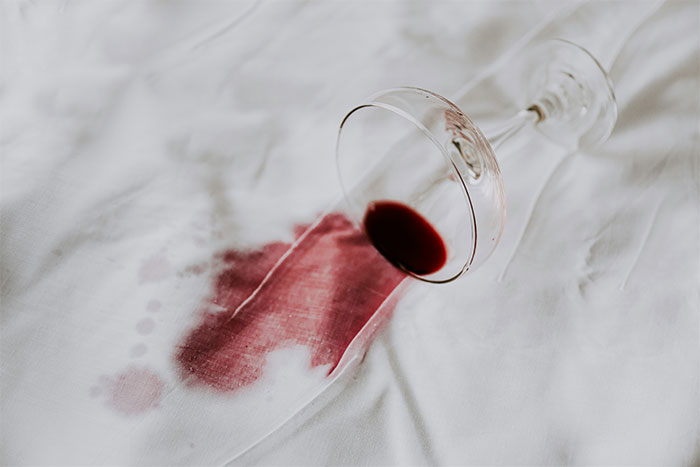 Copa de vino tinto derramada sobre una sábana blanca simbolizando una de las citas terribles presenciadas por camareros.