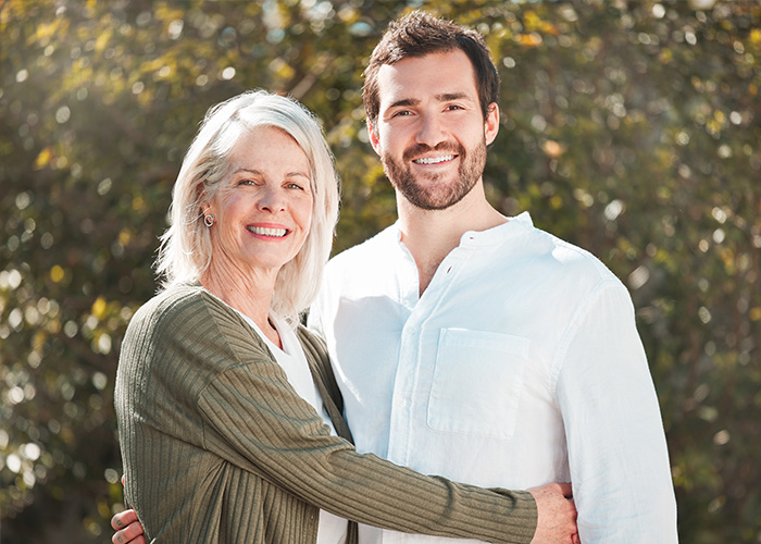 Hombre y su suegra sonrientes abrazados al aire libre, ilustrando relaciones familiares y experiencias con suegras.