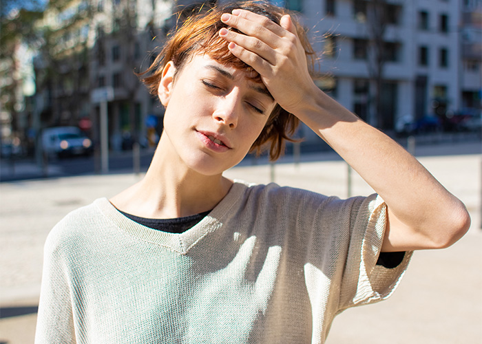 Mujer con presentimiento desagradable, tocándose la frente, al aire libre en un día soleado, mostrando preocupación realista.
