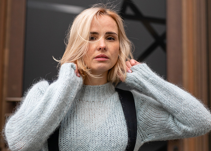 Mujer rubia con suéter gris luciendo pensativa, representando personas con desagradables presentimientos.
