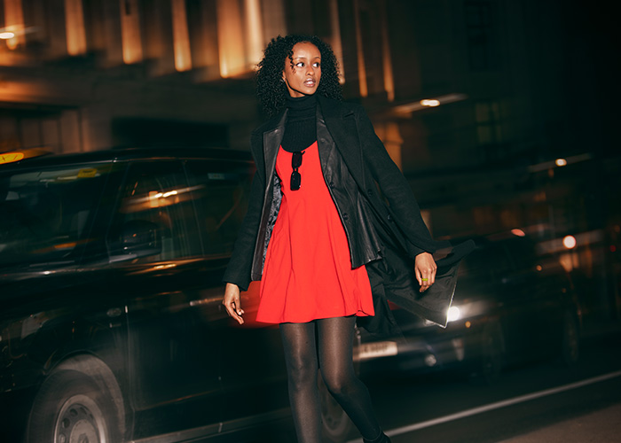 Mujer con vestido rojo y abrigo negro en la calle de noche, reflejando personas con desagradables presentimientos.
