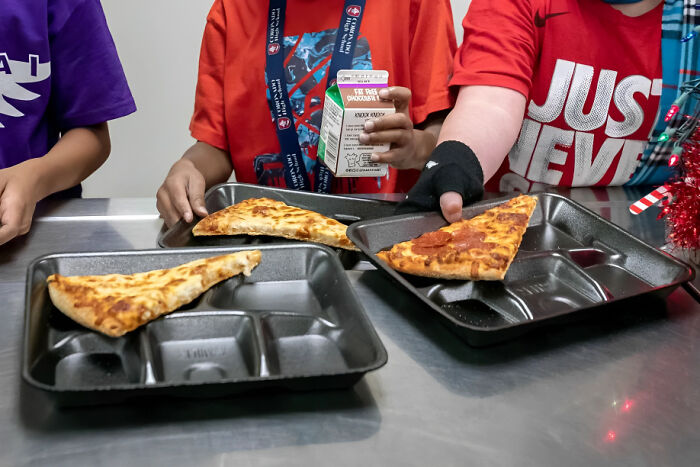 Personas con comportamiento inapropiado en el trabajo sosteniendo bandejas con pizza y bebida en ambiente casual.