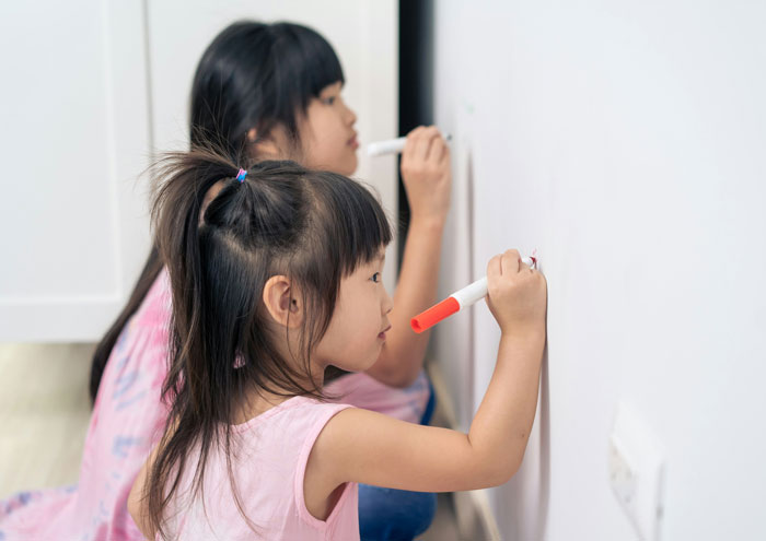 Niñas dibujando en la pared en casa, representando tendencias hogareñas de la vieja escuela superadas por millennials.