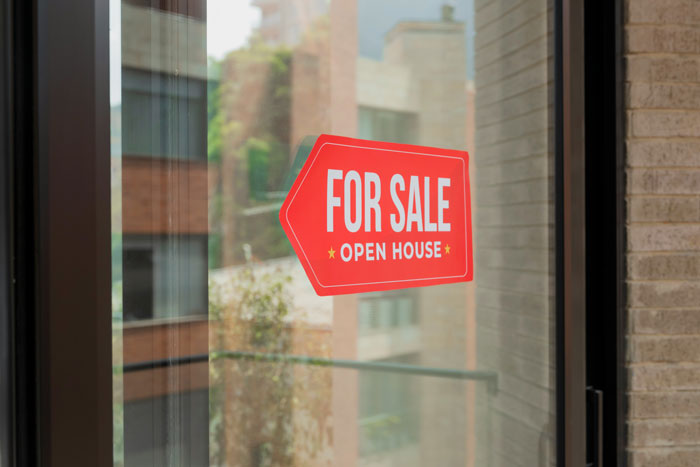 Cartel rojo de venta en ventana de casa reflejando tendencias hogareñas de la vieja escuela superadas por millennials.