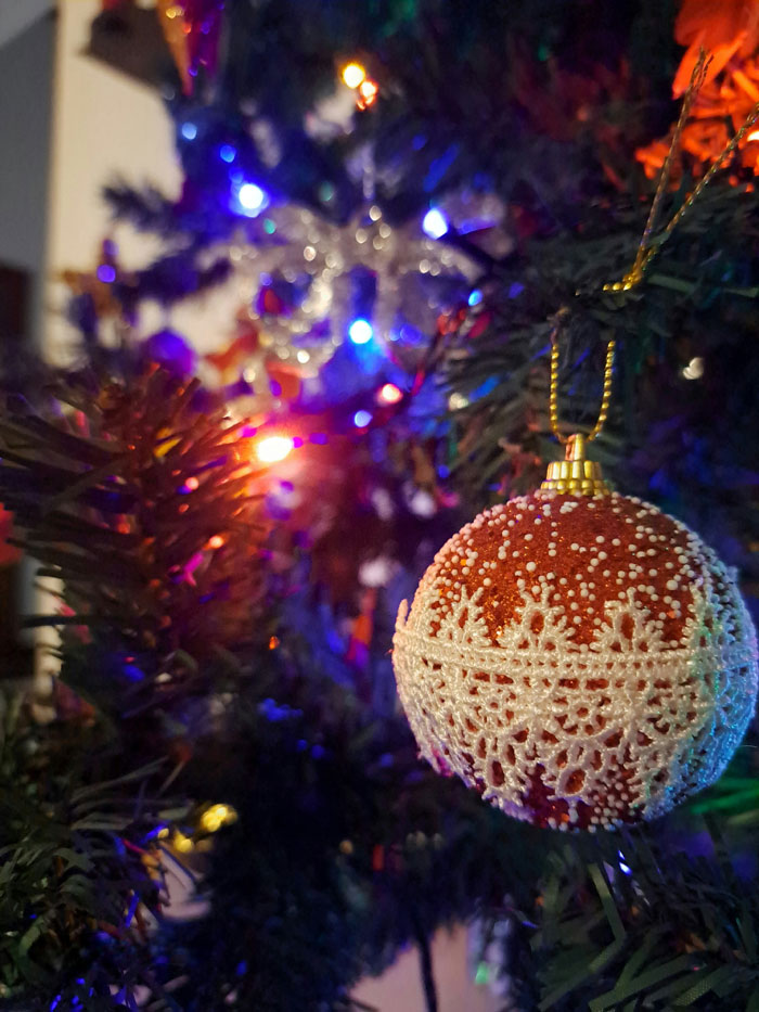 Adorno navideño antiguo colgando en árbol decorado con luces coloridas, representando tendencias hogareñas de la vieja escuela.